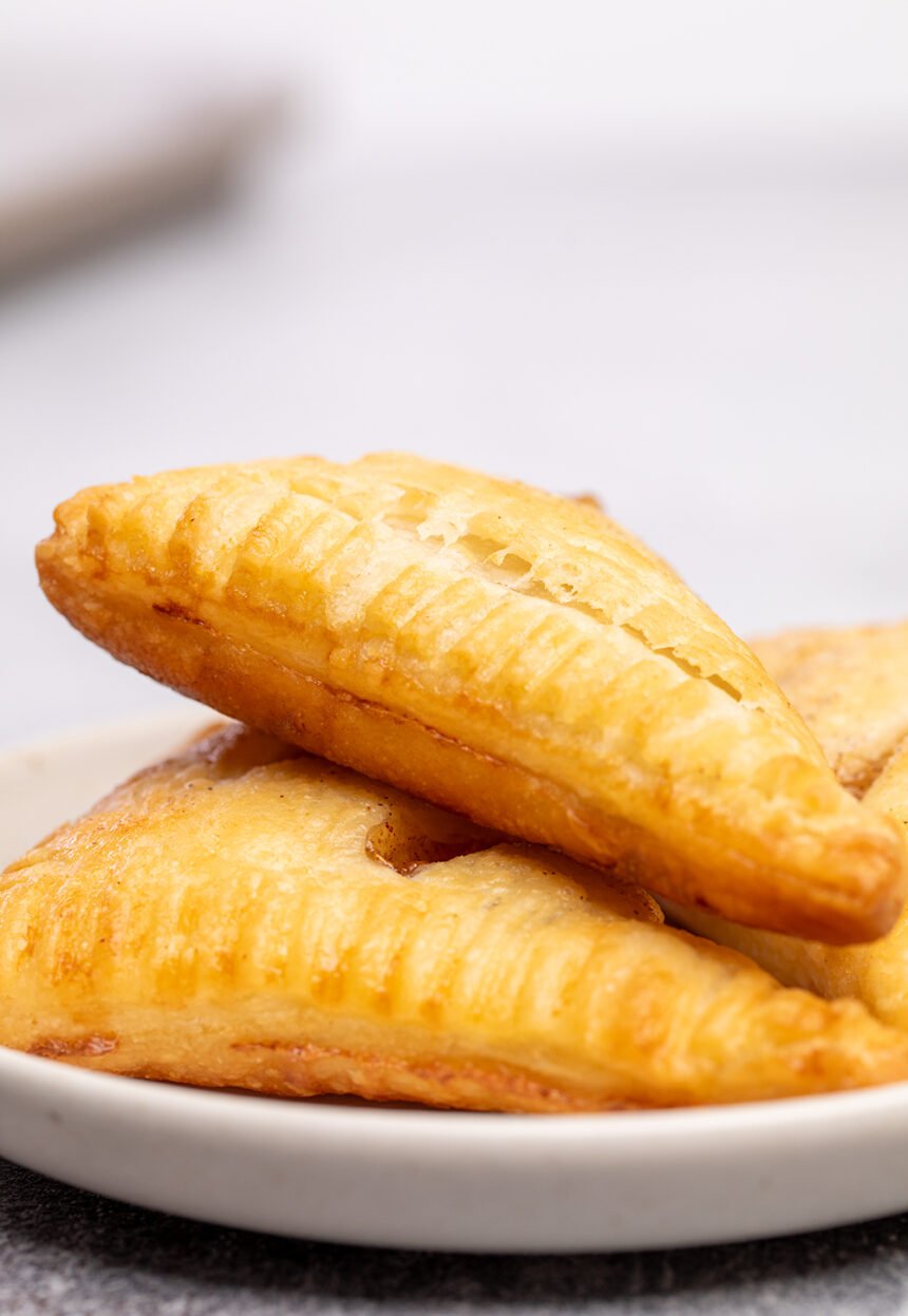 Light brown triangle apple turnovers with puff pastry on small white plate