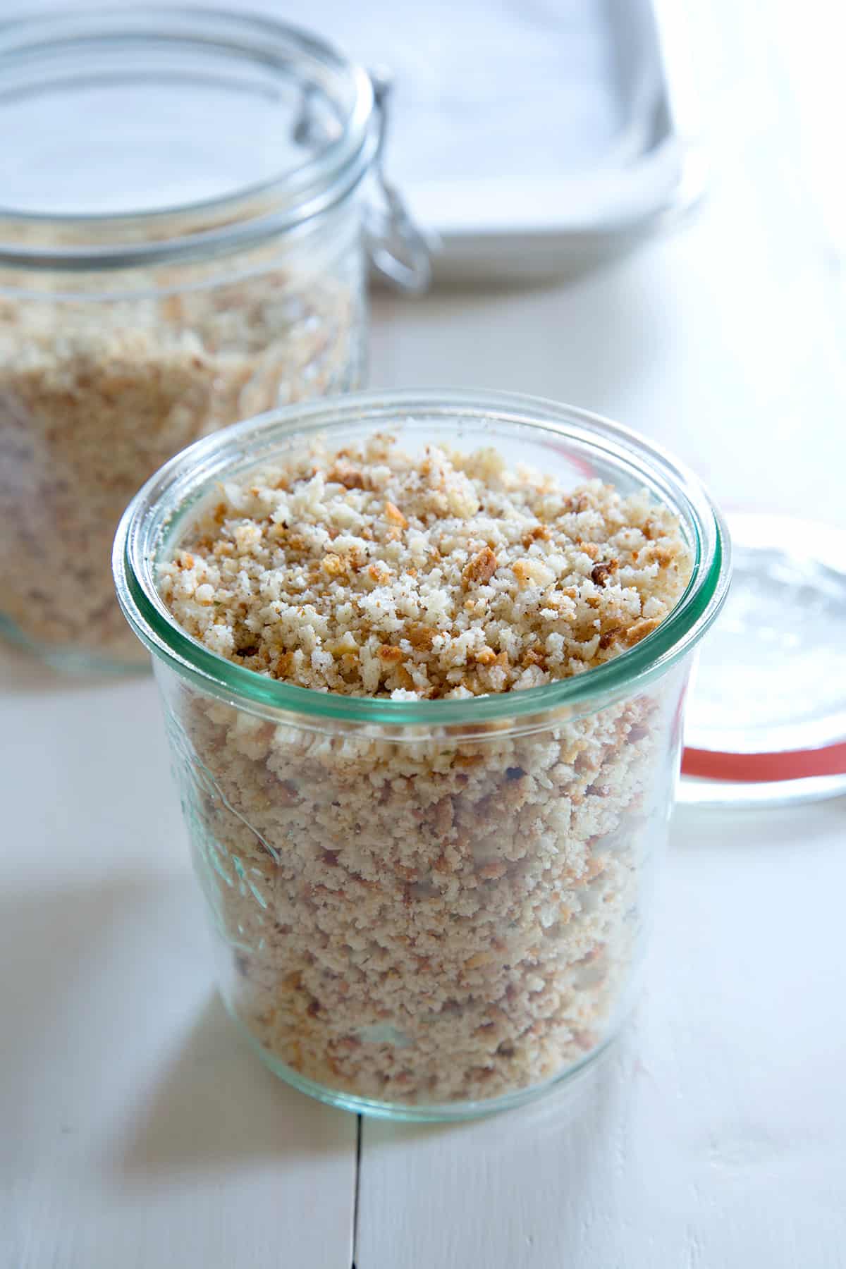 Glass jar of gluten free bread crumbs on white surface.