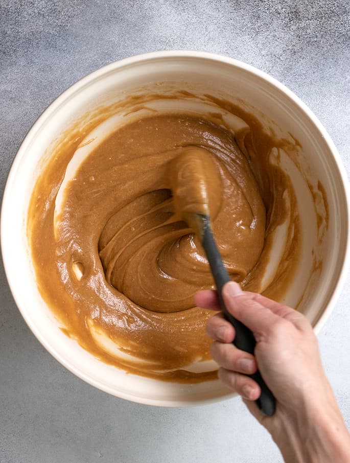 Gingerbread cake batter in a bowl with a hand holding a black spoon stirring