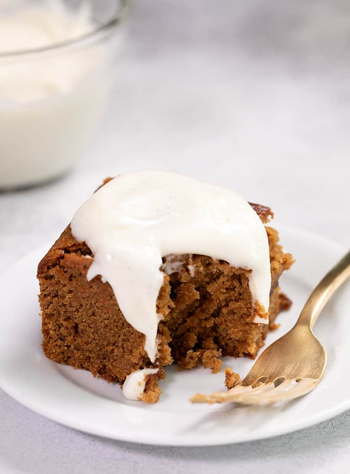 Gingerbread cake with white frosting on small white plate with fork and bite taken