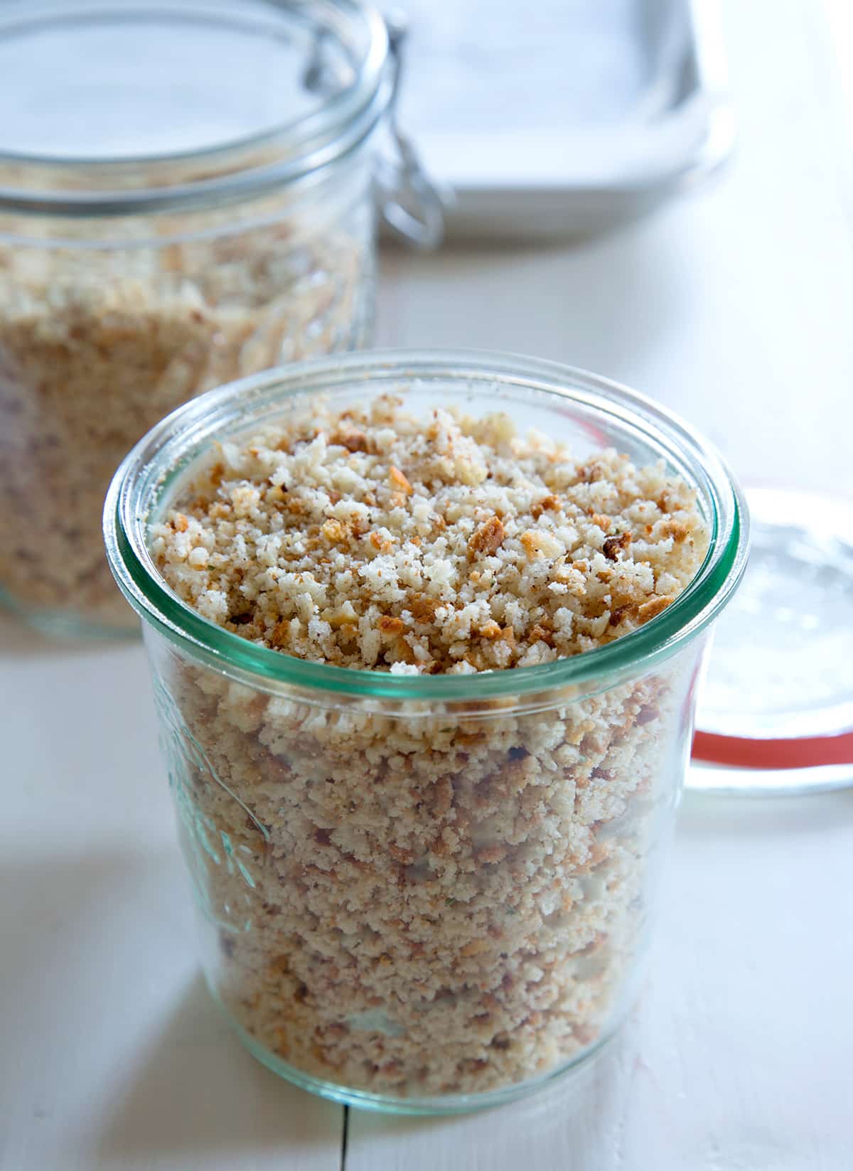 Glass jar of gluten free bread crumbs on white surface.