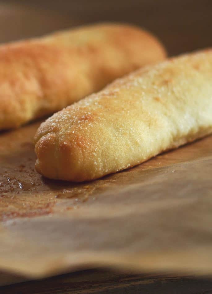 Close up of a breadstick on brown surface with salt on top