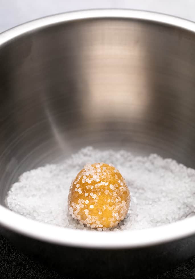 Sugar-coated ball of raw peanut butter cookie dough in metal bowl