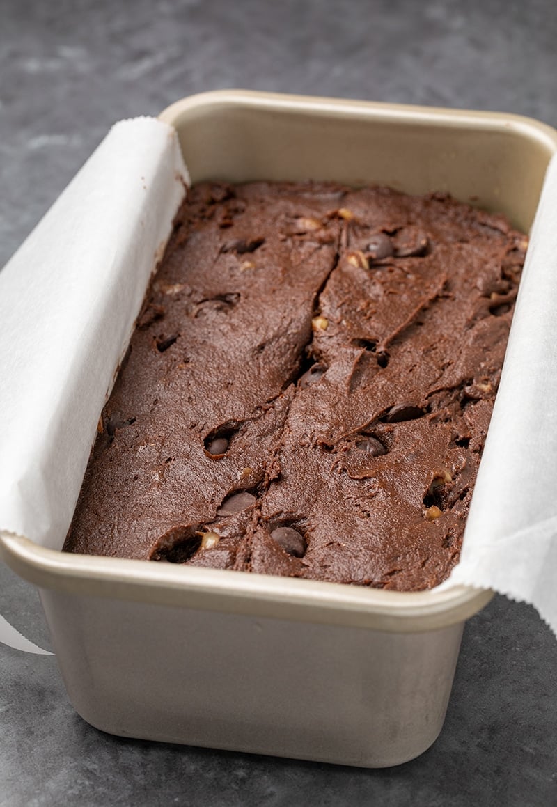 Raw dark brown batter with chips and yellow flecks in white paper in metal loaf pan