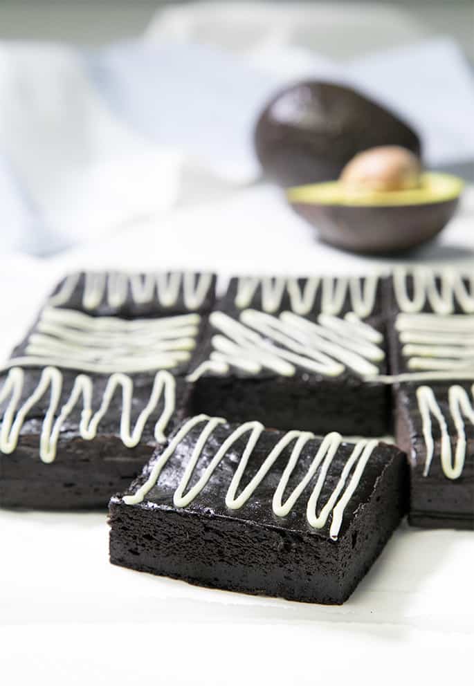 9 avocado brownies with white zigzag pattern on top and avocados on white background