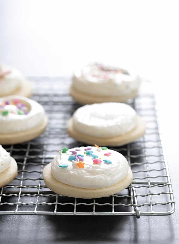 Gluten free sugar cookies decorated with frosting and sprinkles, sitting on rack