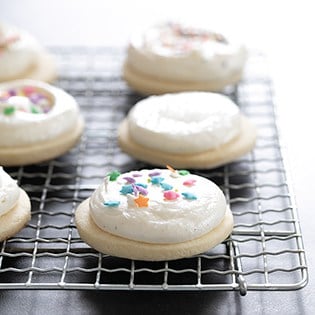 Gluten free soft frosted sugar cookies decorated with sprinkles, sitting on rack