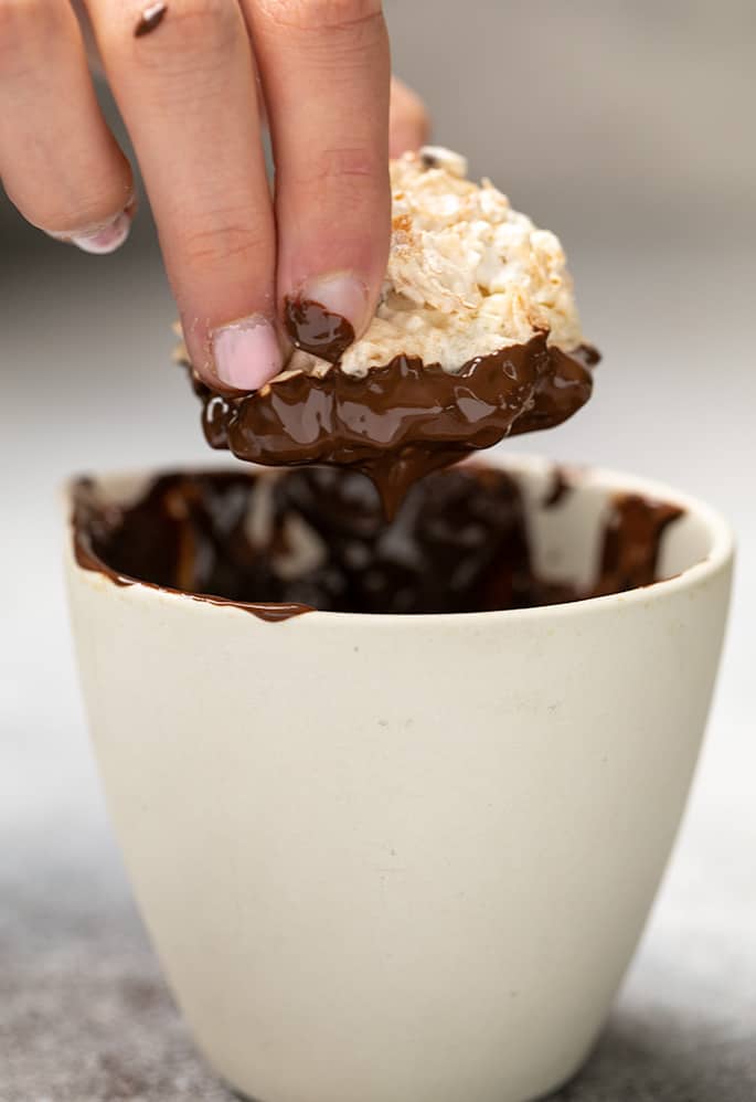 Fingers holding coconut macaroon just dipped in chocolate