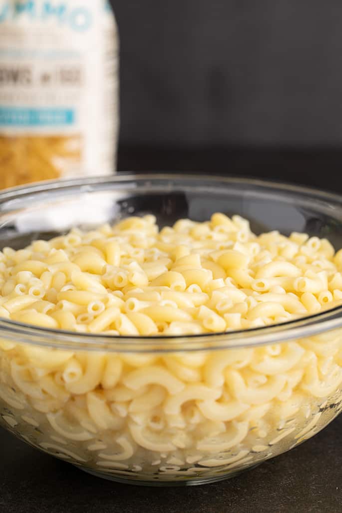 Glass bowl with cooked elbow macaroni with white bag in background