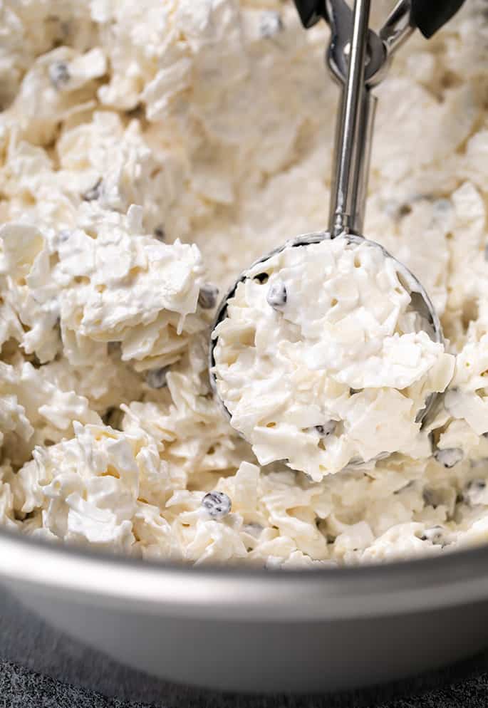 Raw coconut macaroons mixture in metal bowl with some in cookie scoop