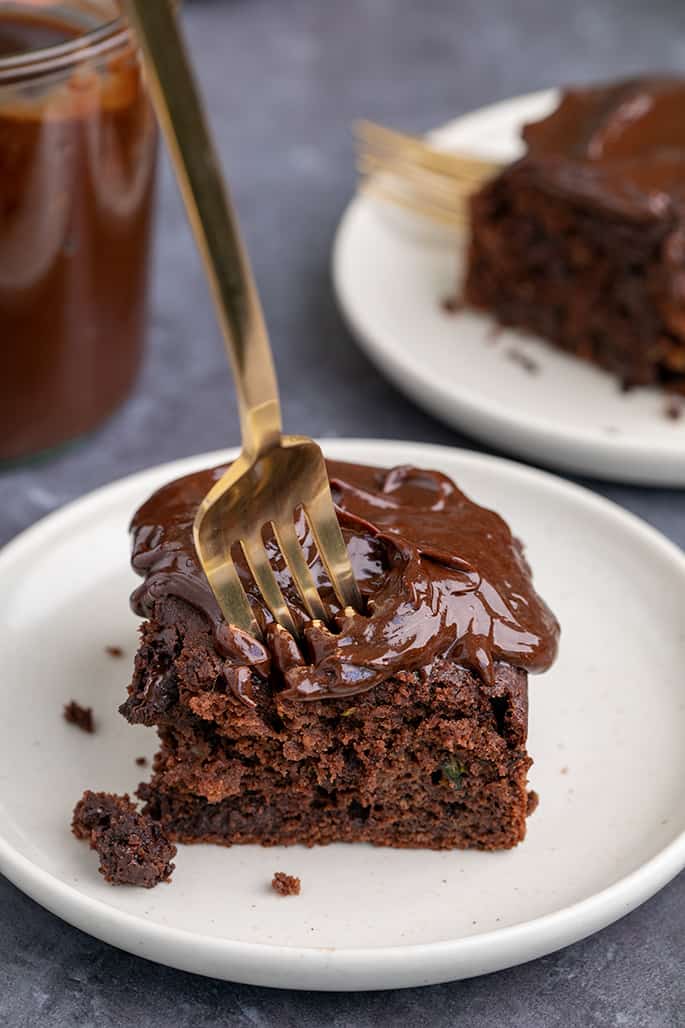 Fork piercing square slice of frosted chocolate cake on small white plate