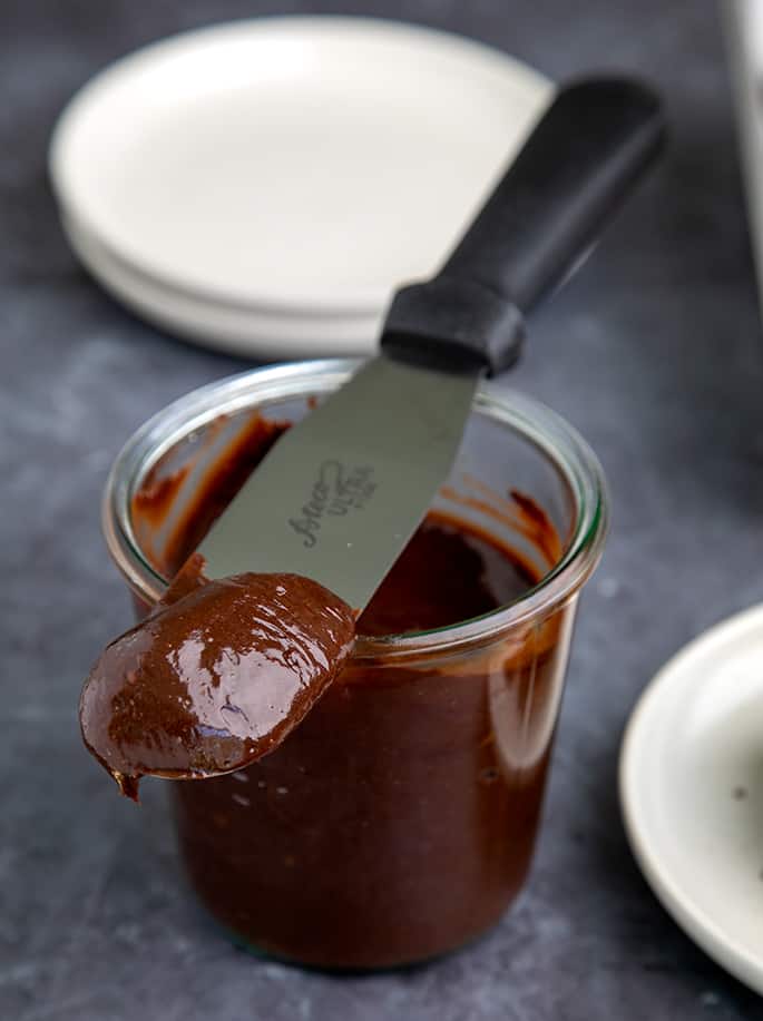 Fudge frosting on end of metal spatula and in glass jar