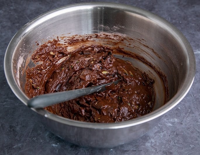 Raw chocolate zucchini cake batter in metal bowl with black spatula