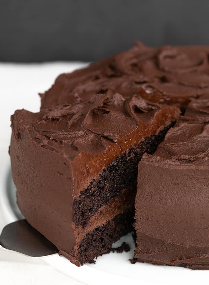 2 layer chocolate cake on white platter with piece being taken out