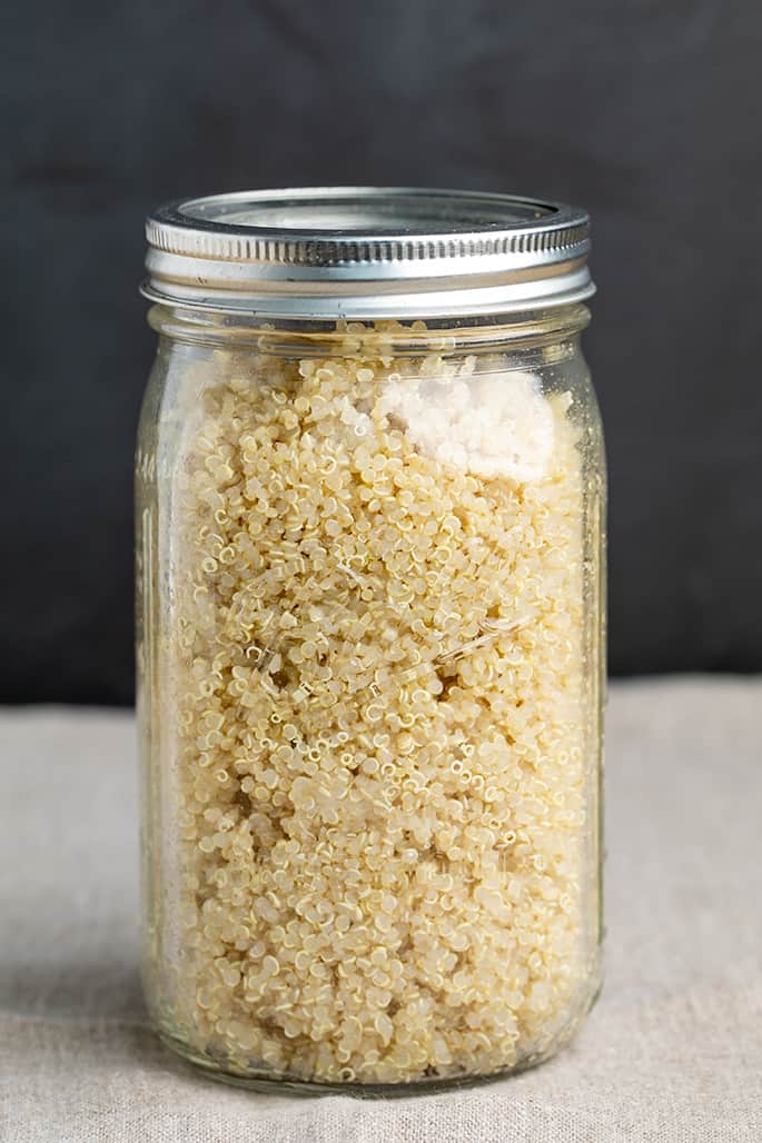 Glass jar with cooked quinoa on tan cloth