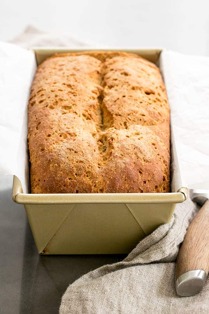 brown crusted loaf of bread split in center in gold loaf pan lined with white paper