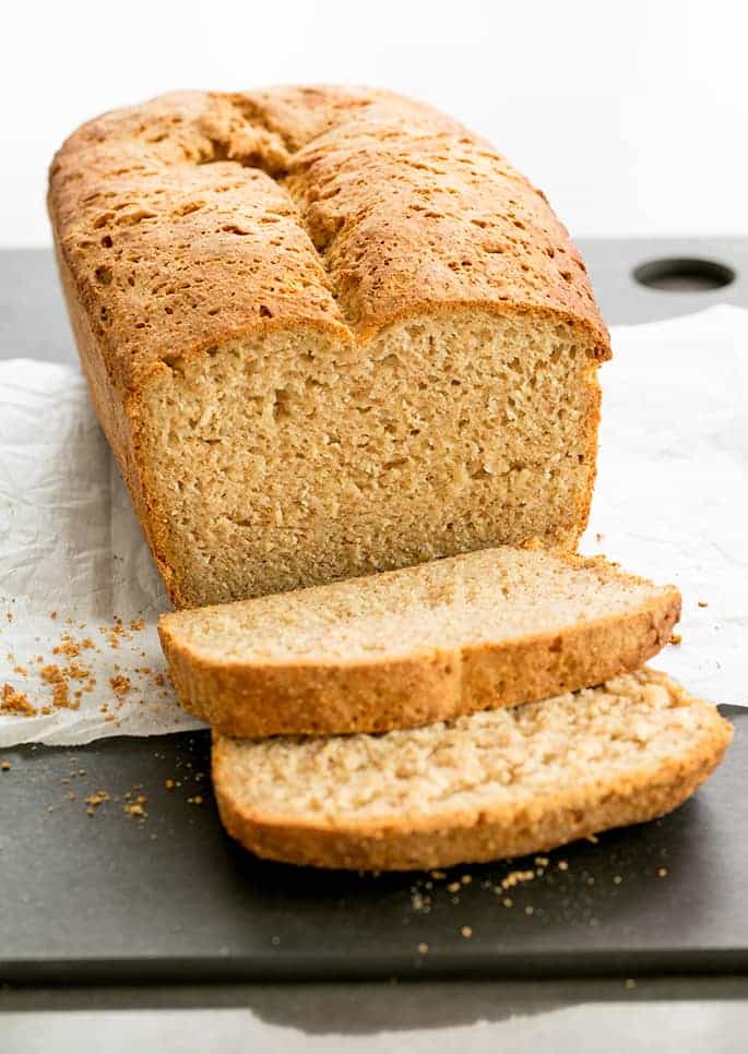 full loaf of brown sandwich bread with two slices cut on white paper with crumbs