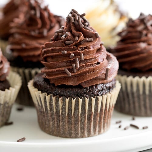 gluten free chocolate cupcakes in brown wrappers with chocolate frosting on white plate