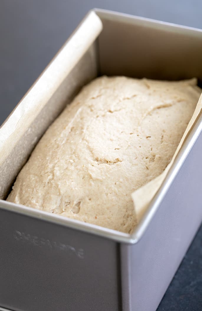 Raw light brown bread dough in pullman pan lined with white paper