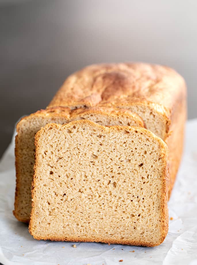 Slice of light brown bread leaning against rest of loaf on white paper