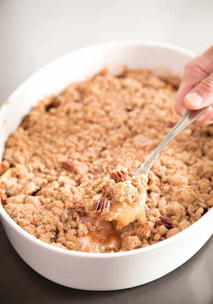 A hand with a spoon and a spoonful of baked gluten free apple crumble