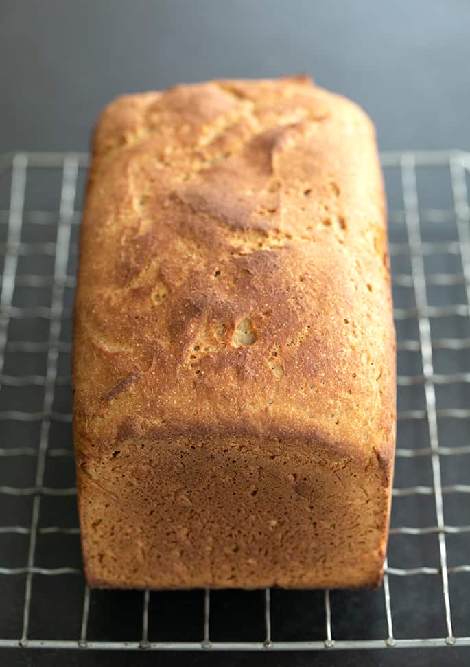 Whole loaf of bread with brown crust on a wire rack on a black table