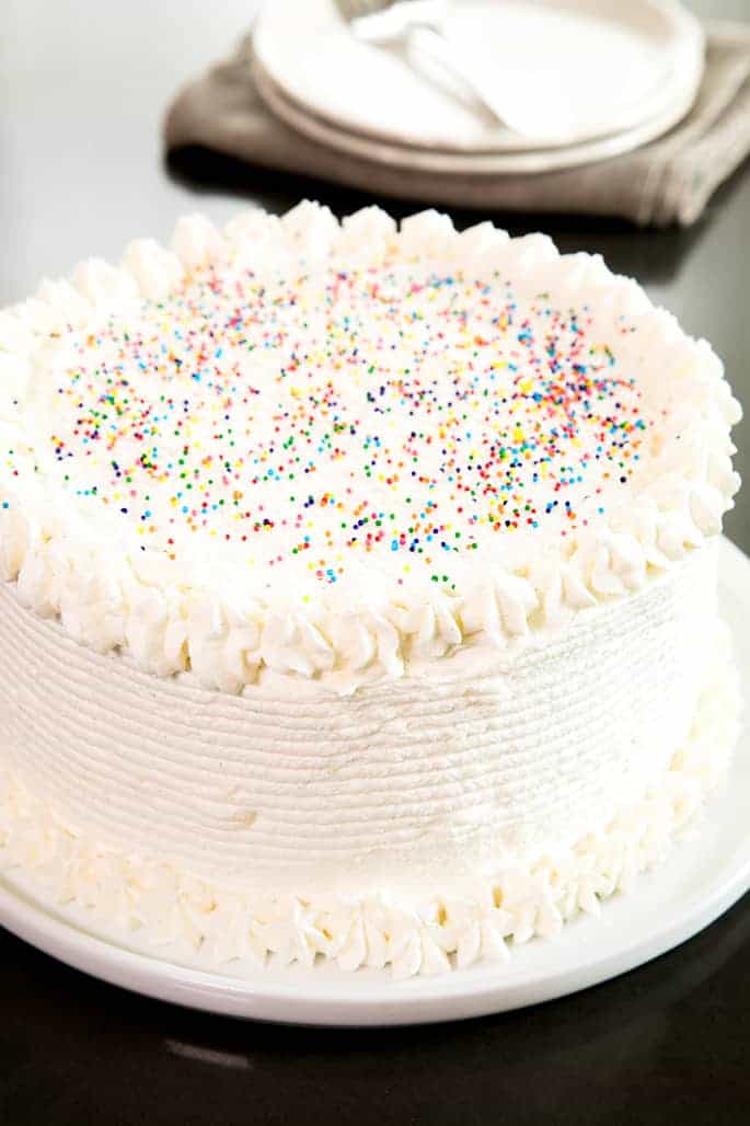 A decorated cake on a plate, with Vanilla ermine frosting and nonpareils