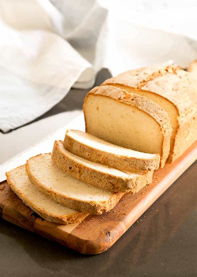 side of sliced white gluten free bread with brown crust on cutting board with white cloth in background