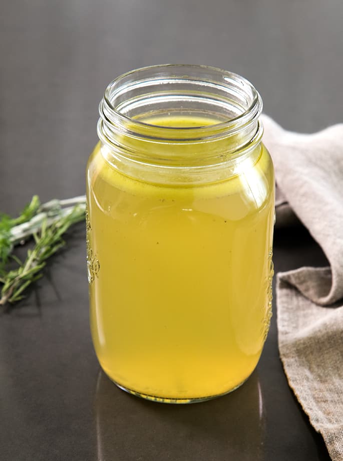 A glass jar of chicken stock on a table