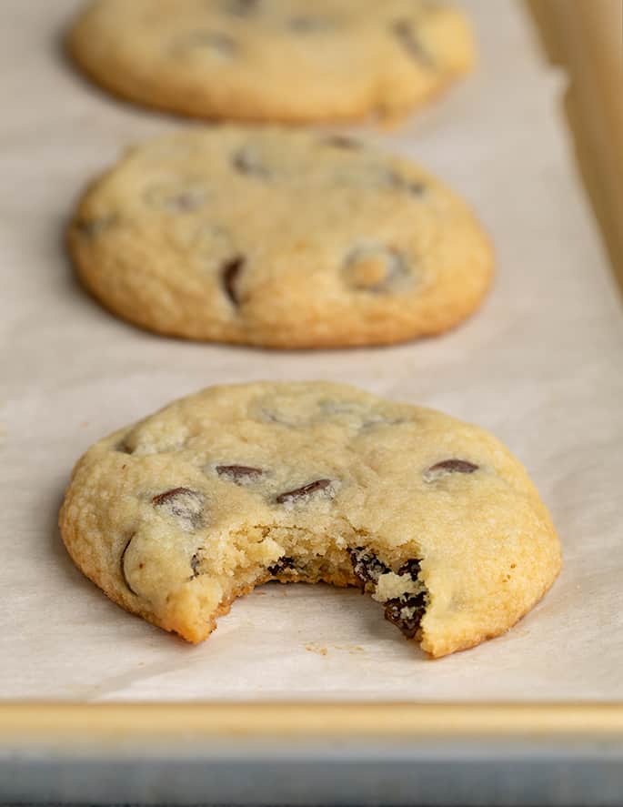 Bitten soft chocolate chip cookies on white paper on baking tray with whole cookies behind it