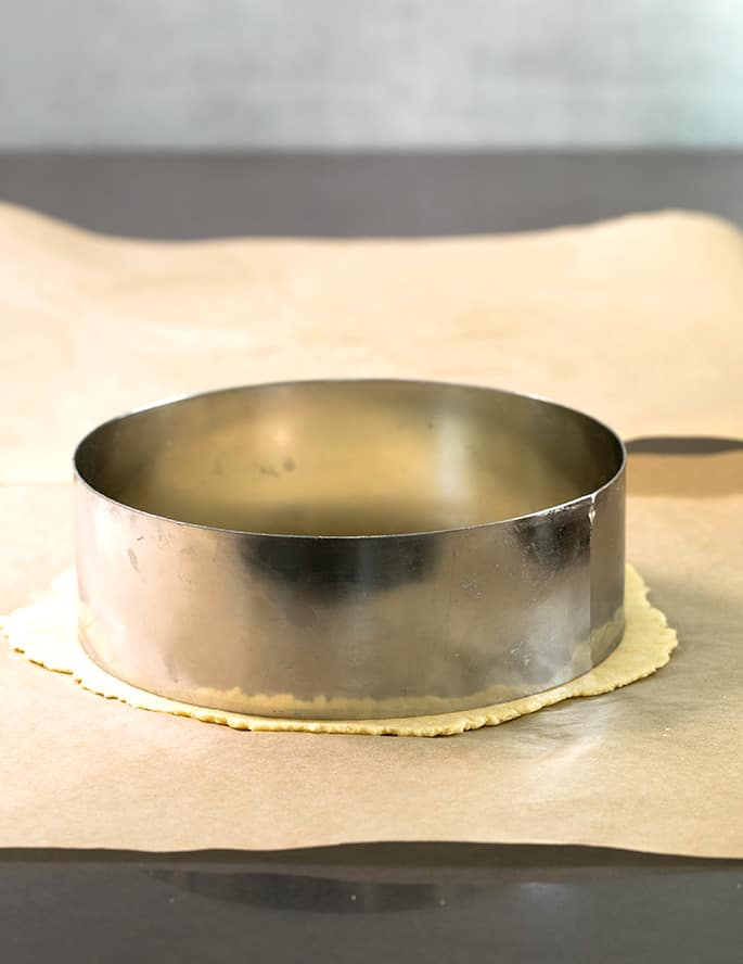 round metal cake cutter pressing a perfect circle into thin light yellow almond flour tortilla dough on brown paper