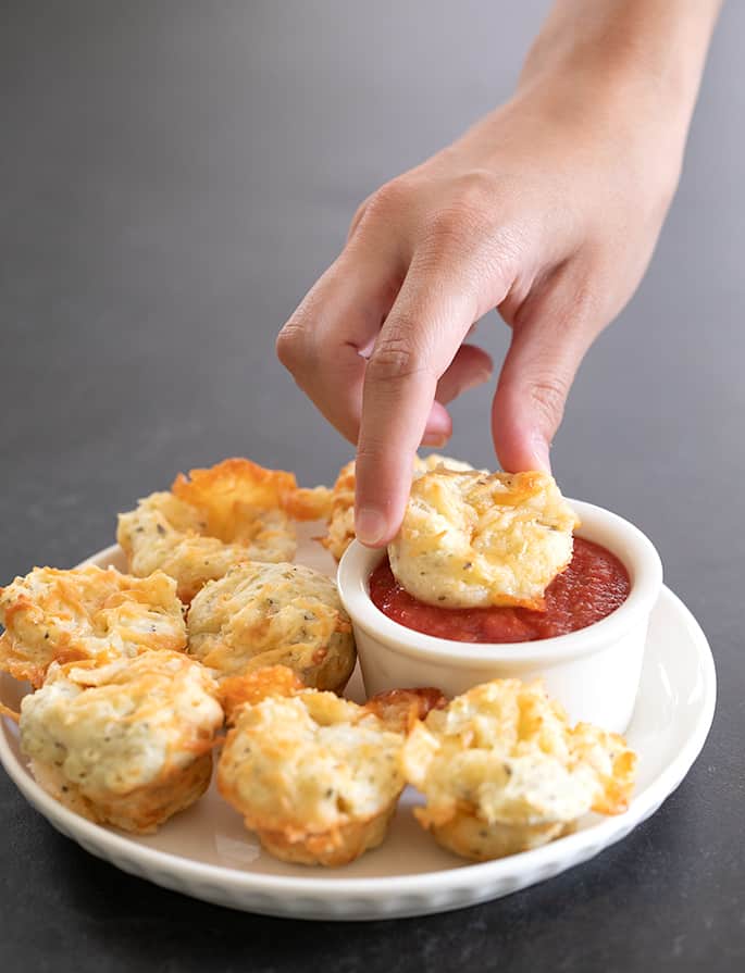 Hand dipping mini pizza bite in sauce