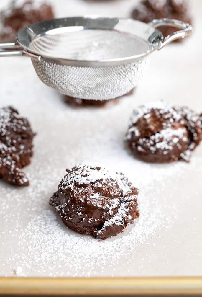 Sifter with sugar positioned over mounds of raw chocolate cookie dough