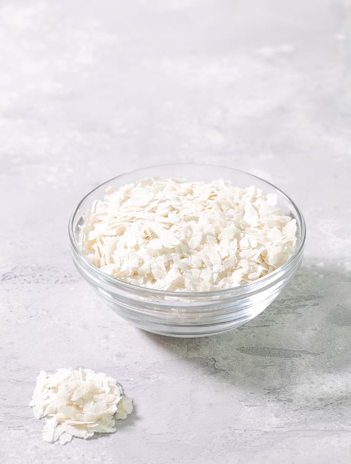 A small glass bowl with white flakes of flattened rice in a light gray background