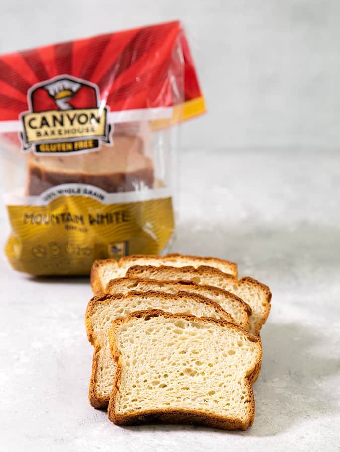 5 slices of baked bread on a light gray surface with a plastic bread package with the name Canyon Bakehouse Gluten Free Mountain White