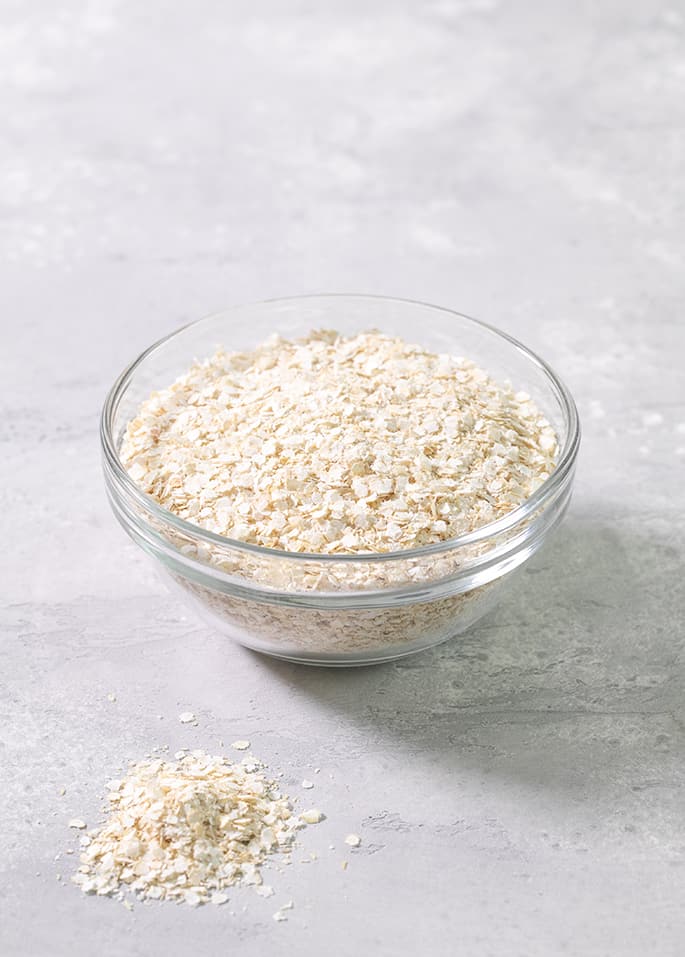 A glass bowl of quinoa flakes on a gray table