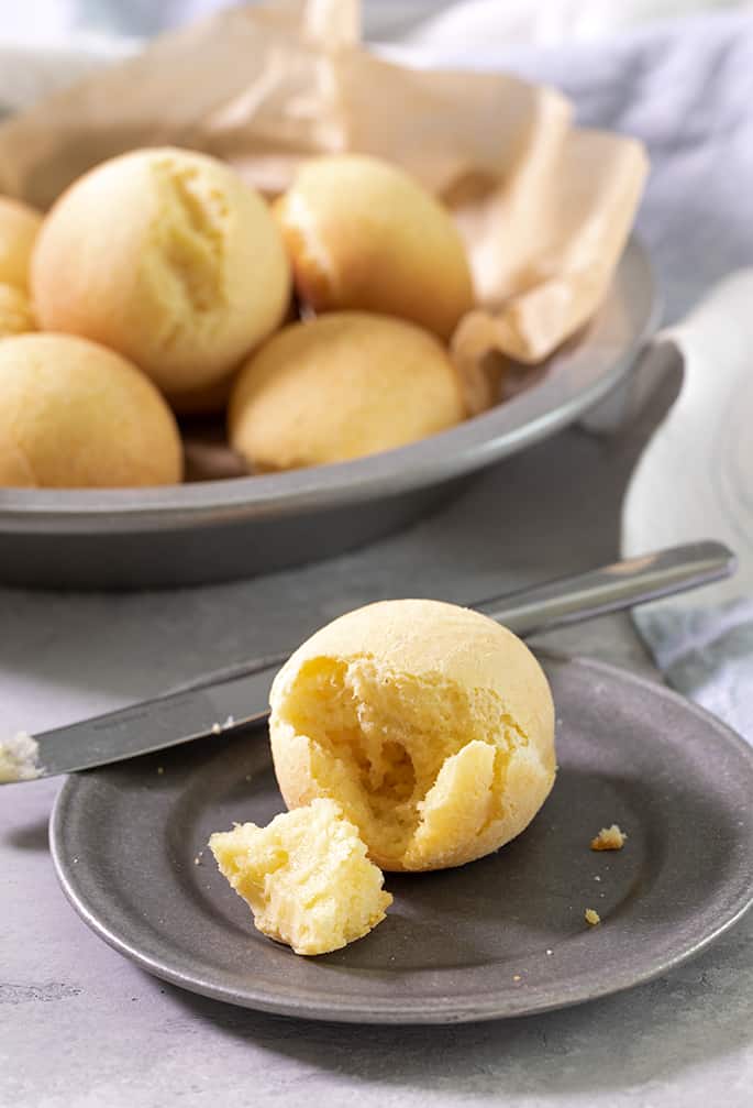 A small plate with pan de bono broken, with a butter knife