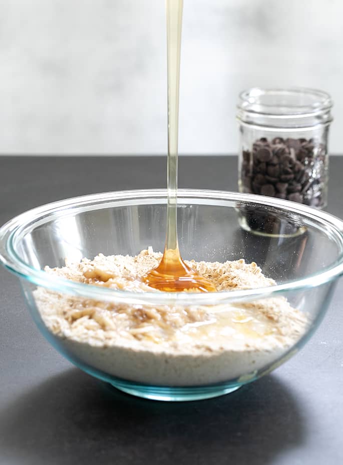 A bowl of dry ingredients with honey pouring in