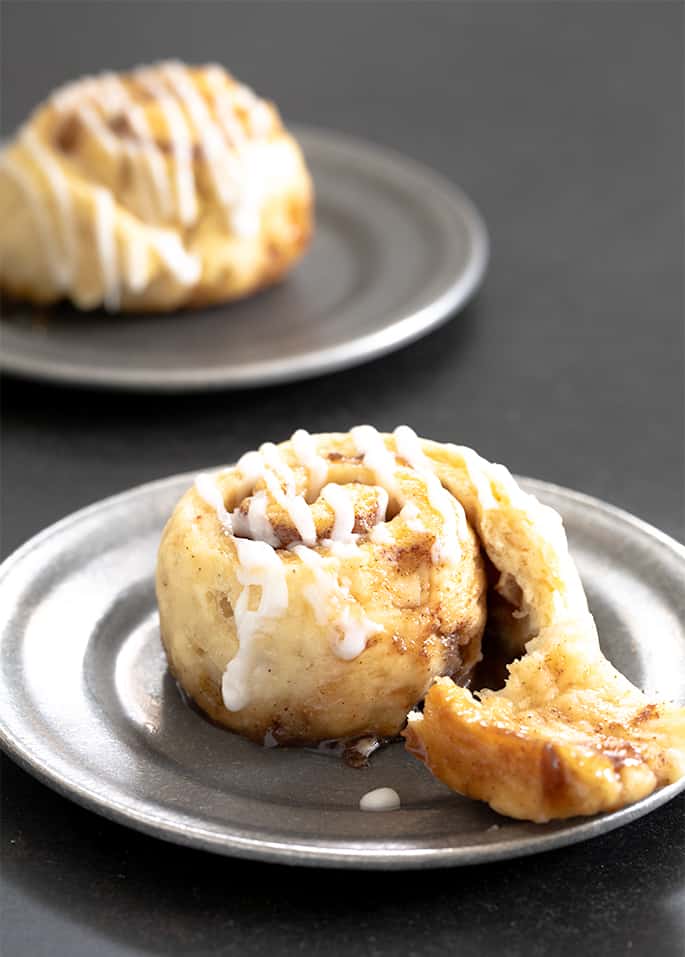 a partially uncoiled brown round baked roll with melted brown sugar and drizzled white icing on a small round metal plate