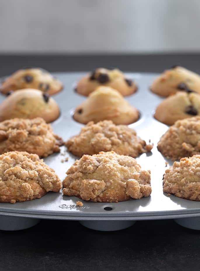 Closeup sideview of light colored crumble topping on gluten free muffins in metal muffin tin