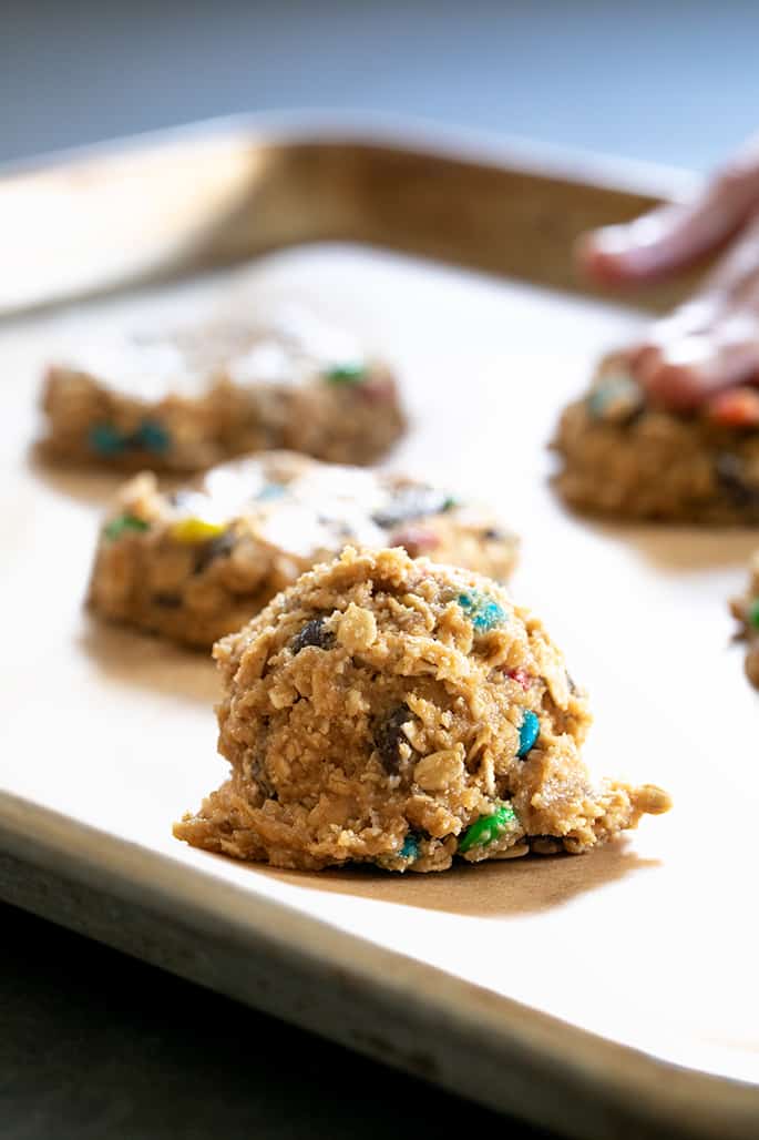 Small mound of light brown cookie dough with colored candy pieces and oats on brown paper-lined metal baking tray