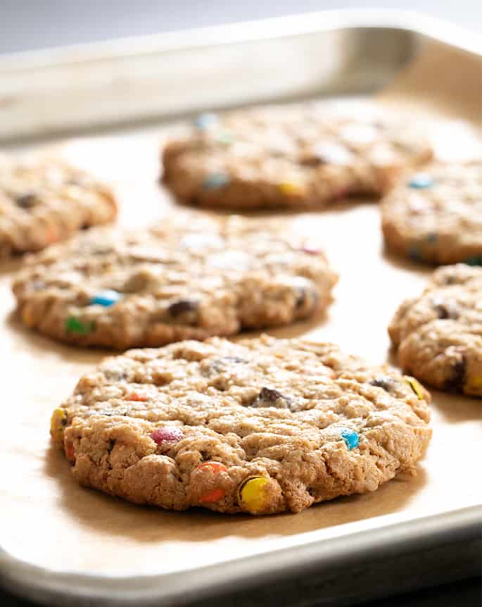 Closeup image of round light brown cookie with brightly colored candy pieces on brown paper lined metal tray