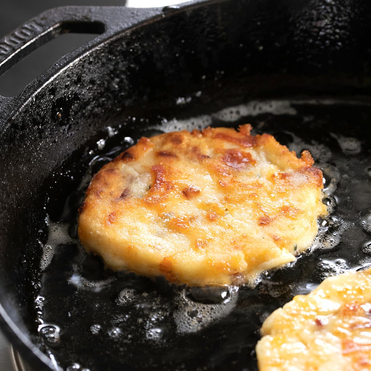 round cakes of fried mashed potatoes frying in black cast iron skillet