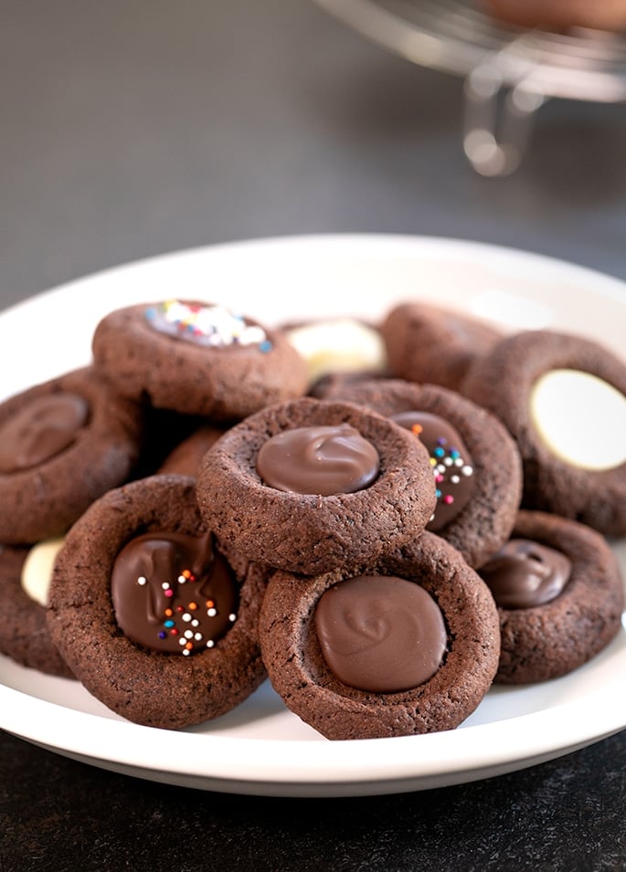 A plate of chocolate thumbprint cookies with chocolate filling on a platter