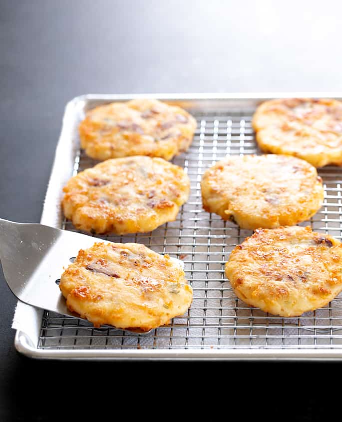 Metal spatula placing fried mashed potatoes on wire rack on top of lined baking sheet