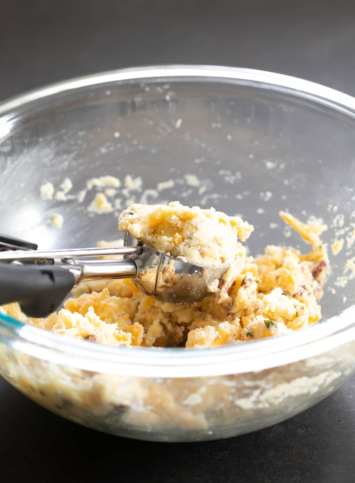 Spring loaded ice cream scoop with light yellow mashed potato mixture in glass mixing bowl