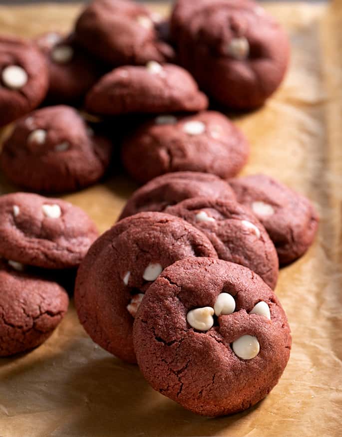 Front facing image of red round drop cookies with white chocolate chips on top on brown paper