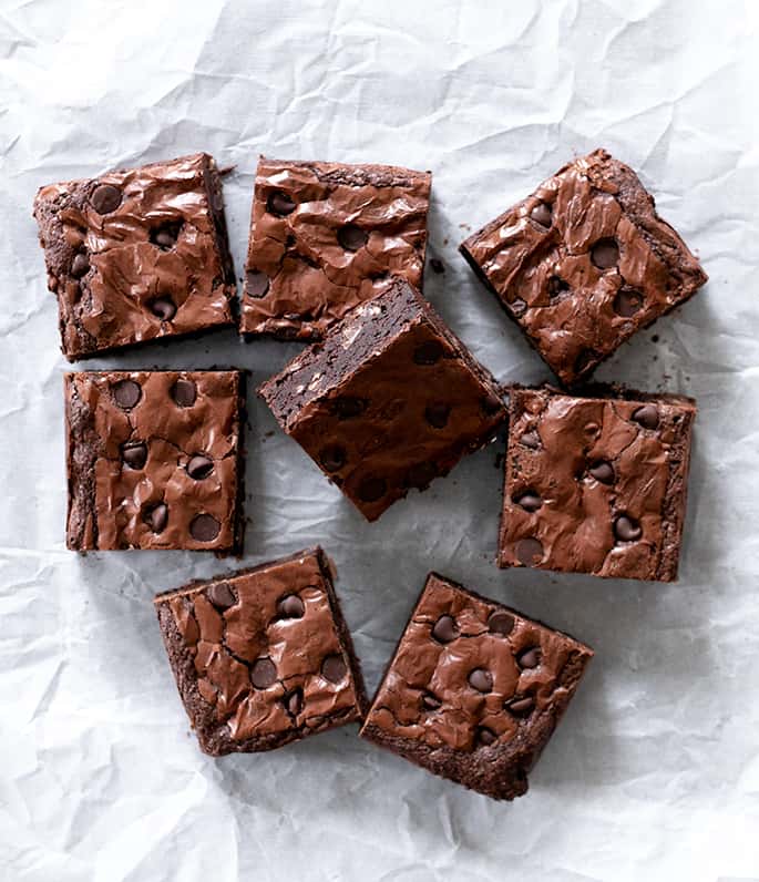 Overhead image of 8 brown bar squares with chocolate chips on white crinkly paper