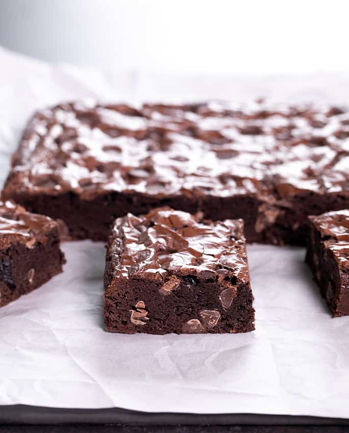 White crinkled paper underlying brown bars with chocolate chips, some sliced into squares