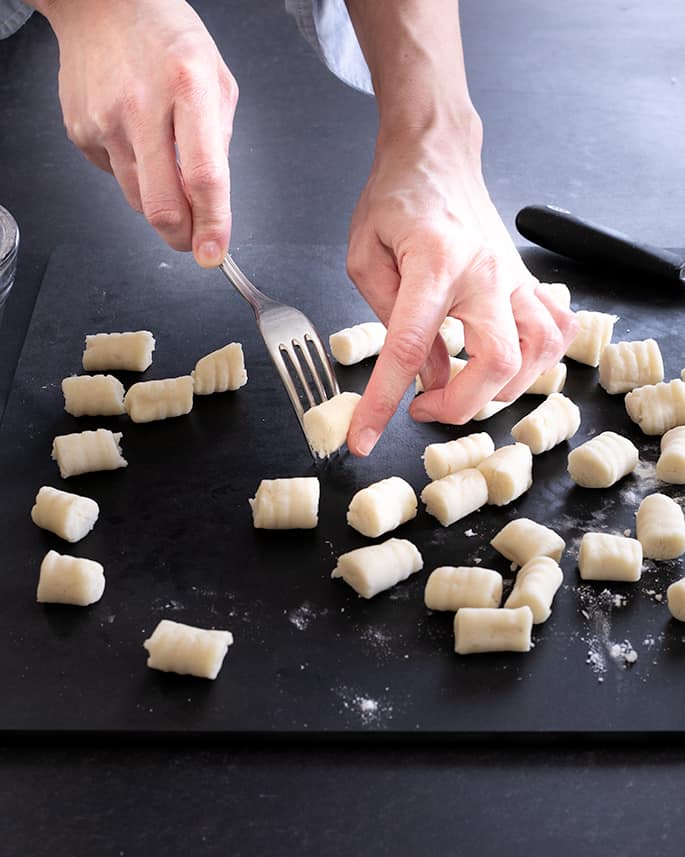 fingers shaping 1-inch dumpling dough on the back of a fork on a black surface